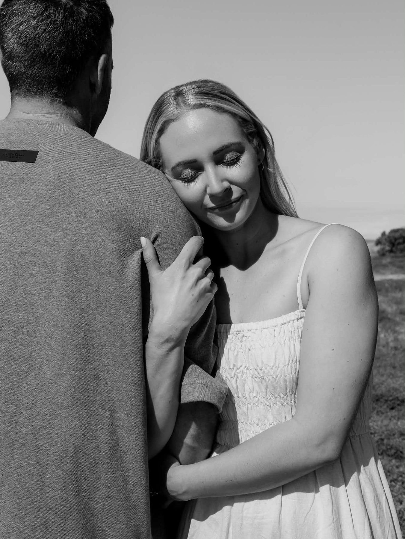 Black-and-white photograph of Lacy resting her head on Josh's shoulder, eyes closed and smiling